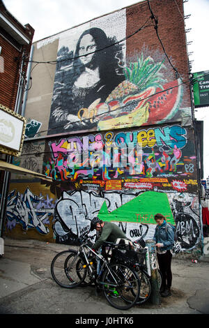 Kanada, Toronto. Kensington Market, multikulturellen Nachbarschaft. Ein paar schloss ihre Fahrräder vor einer bemalten Wand mit Mona Lisa und Graffiti. Stockfoto