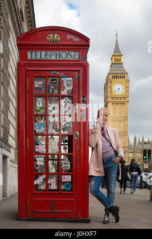 Lässige blonde Frau am Handy in London, stützte sich auf traditionelle britische rote Telefonzelle. Big Ben im Hintergrund zu sehen. London, Stockfoto