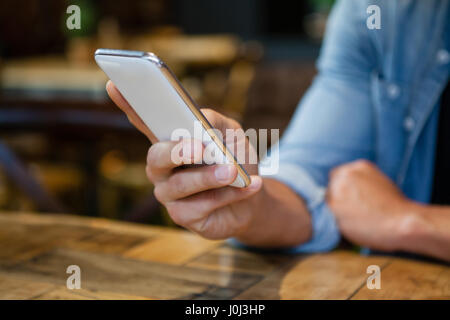 Bild des Mannes mit Smartphone beim Sitzen am Tisch im Café beschnitten Stockfoto