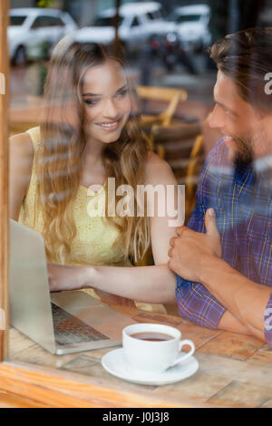 Lächelnde paar mit digitalen Laptop sitzen im Café Shop gesehen durch Glasfenster Stockfoto