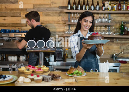 Porträt von lächelnden Kellnerin hält einen Schokoladenkuchen am Schalter im CafÃƒÂ © Stockfoto