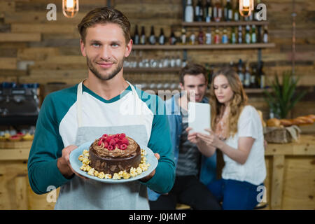 Porträt von Kellner Halteplatte an Kuchen und Kunden im Hintergrund im café Stockfoto