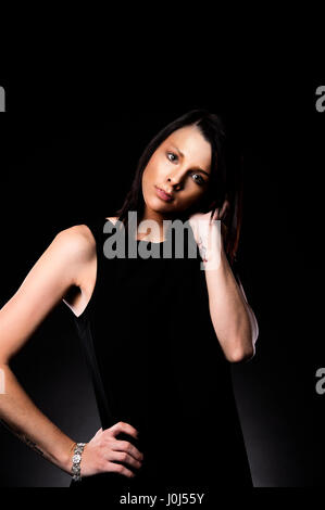 Schlanke dunkelhaarige Frau trug ein schwarzes ärmelloses Kleid mit ihrer linken Hand durch ihr Haar Stockfoto