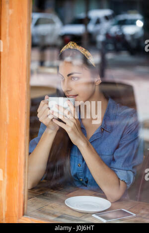 Nachdenkliche Frau trinkt Kaffee sitzend am Tisch im Café shop Stockfoto