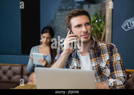 Junger Mann telefonieren mit Handy während mit Laptop in CafÃƒÂ © Stockfoto