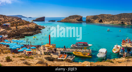 Comino, Malta - Touristen Menschenmenge bei Blue Lagoon, das klare türkisfarbene Wasser an einem sonnigen Sommertag mit klaren, blauen Himmel und Boote auf Comino Insel zu genießen, Stockfoto