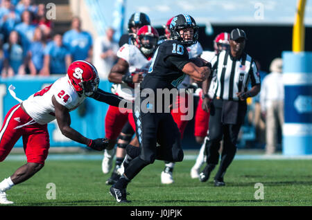 North Carolina Tar Heels Quarterback Mitch Trubisky (10) entzieht sich den Griff der North Carolina State Wolfpack Sicherheit Shawn Boone (24) in der ersten Hälfte von der NCAA Football-Spiel zwischen den North Carolina Tar Heels und der NC State Wolfpack Kenan Memorial Stadium in Chapel Hill. Stockfoto