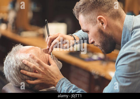 Junge Meister rasieren Bart des Clients im Frisörsalon Stockfoto