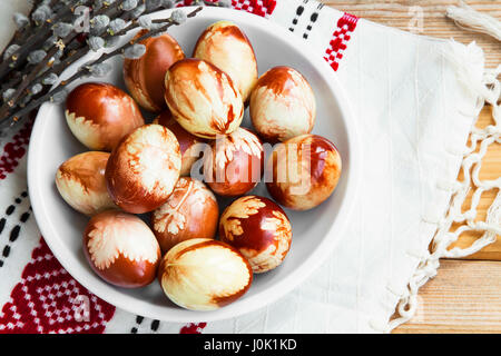 Ostereier bemalt traditionell mit verschiedenen Kräutern und Blättern in einem Teller mit Frühjahr Knospen und traditionelle Hand-Nähen-Handtuch Stockfoto