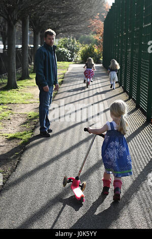 Kinder spielen auf Motorroller und Fahrräder, Fahrradverleih in Herbert Park, Dublin Irland Vater Tochter Konzept Stockfoto