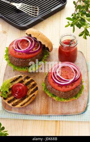 Burger mit Salat Tomate rote Zwiebel auf gegrillte Brötchen mit ketchup Stockfoto