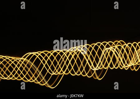 Licht Malerei Fotografie mit gold Lichterketten, vor einem schwarzen Hintergrund. Lange Belichtung Foto, lebendige metallische Farbe gelb, wirbelnden Muster Stockfoto
