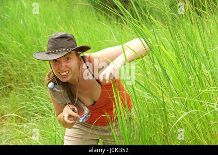 Eine Kaukasische Frau versteckt sich in langen Dschungel Rasen vorgibt, ein unheimlich Tier Stockfoto