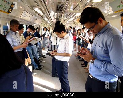 Singapur - 22. Dezember 2015: Pendler oder Insassen der MRT vorbei die Zeit spielen, Videos ansehen, ihre e-Mails checken oder Aktualisierung Stockfoto