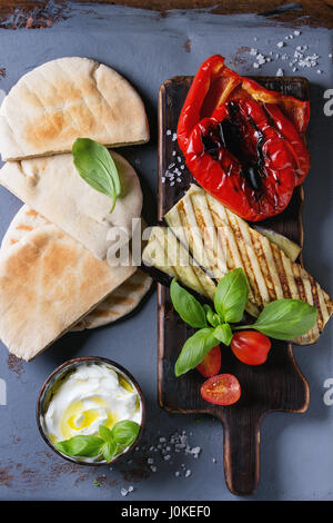 Zutaten für die Herstellung von Pita Brot Brötchen. Gegrilltes Gemüse, Basilikum und Feta-Käse mit Fladenbrot auf hölzernen Portion Brett über graue Textur Rücken Stockfoto