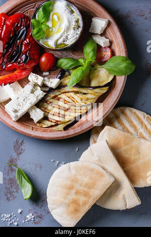 Zutaten für die Herstellung von Pita Brot Brötchen. Gegrilltes Gemüse, Basilikum und Feta-Käse mit Fladenbrot auf Terrakotta Teller über graue Textur staatlich Stockfoto