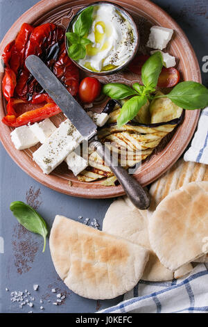 Zutaten für die Herstellung von Pita Brot Brötchen. Gegrilltes Gemüse, Basilikum und Feta-Käse mit Fladenbrot auf Terrakotta Teller über graue Textur staatlich Stockfoto