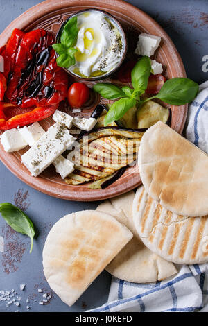 Zutaten für die Herstellung von Pita Brot Brötchen. Gegrilltes Gemüse, Basilikum und Feta-Käse mit Fladenbrot auf Terrakotta Teller über graue Textur staatlich Stockfoto