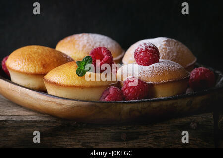 Hausgemachte Zitronen Muffin Muffins mit frischen Himbeeren, Zucker Pulver, Minze, in quadratische Holzplatte auf Holztisch auf dunklem Hintergrund serviert. Dunklen Rost Stockfoto
