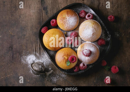 Hausgemachte Zitronen Muffin Muffins mit frischen Himbeeren, Zucker Pulver, Minze, serviert in quadratische Holzplatte mit Vintage Sieb über alten dunklen hölzernen Hinterg Stockfoto