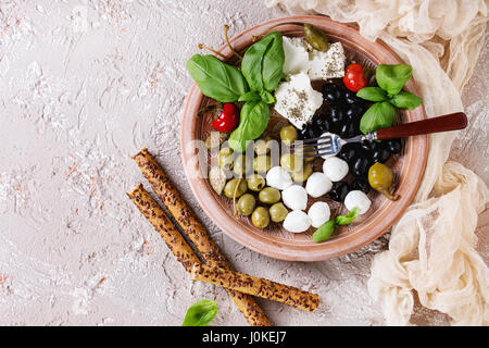 Mediterrane Vorspeise Antipasti Teller mit grünen und schwarzen Oliven, Feta-Käse, Mozzarella, Kapern, Pfeffer, Basilikum mit Grissini Brot hält sich über beige Stockfoto