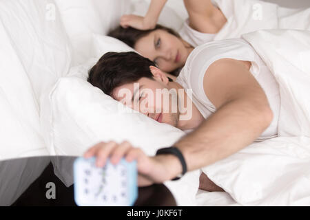 Verschlafene wütend paar im Bett, der Wecker ausschalten Stockfoto