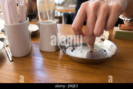 Hand eine Zigarette im Aschenbecher auf einem Holztisch Außerbetriebnahme. Stockfoto