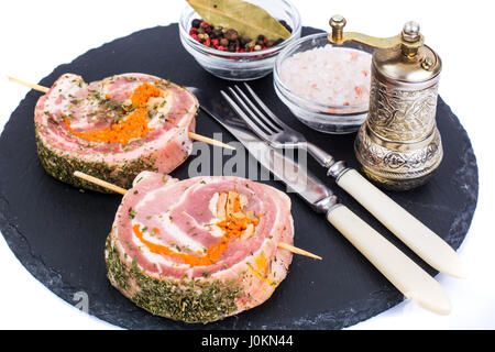 Rolle Schweinefleisch mit Gewürzen zum Grillen auf schwarzem Stein. Studio Photo Stockfoto