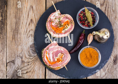 Rolle Schweinefleisch mit Gewürzen zum Grillen auf schwarzem Stein. Studio Photo Stockfoto