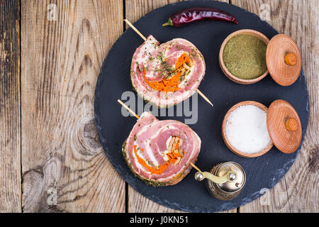 Rolle Schweinefleisch mit Gewürzen zum Grillen auf schwarzem Stein. Studio Photo Stockfoto