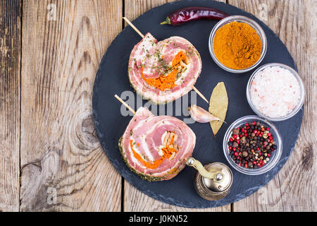 Rolle Schweinefleisch mit Gewürzen zum Grillen auf schwarzem Stein. Studio Photo Stockfoto