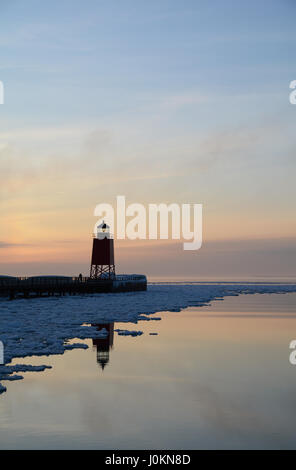 Ein Leuchtturm spiegelt sich in dem ruhigen Wasser des Lake Michigan bei Sonnenuntergang im Winter. Stockfoto