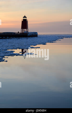 Ein Leuchtturm spiegelt sich in der Ruhe Schnee und Eis gefüllt Wasser des Lake Michigan bei Sonnenuntergang im Winter. Stockfoto