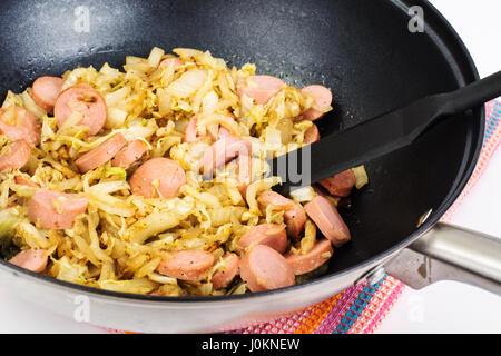 Gedünsteter Kohl mit Würstchen in Pfanne auf weißem Hintergrund. Studio Photo Stockfoto