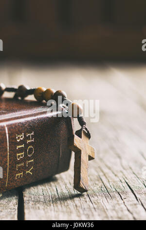 Rosenkranz und Heilige Bibel auf Holztisch. Stockfoto