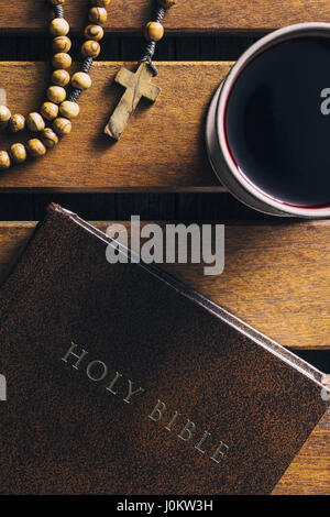 Rosenkranz, Bibel und Becher Wein auf Holztisch. Ansicht von oben. Stockfoto