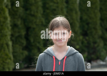 Hübsche elfjährigen Mädchen im freien Blick in die Kamera vor grünen Zypresse Stockfoto