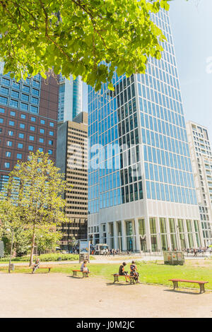 Mitarbeiter, die ein Mittagessen brechen im öffentlichen Park Taunusanlage mit Bürogebäude im Hintergrund Stockfoto