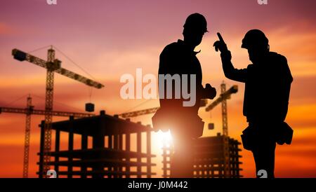 Gewerbebau-Konzept mit Silhouette zweier Arbeiter tragen Schutzhelme und Baustelle im Hintergrund. Stockfoto