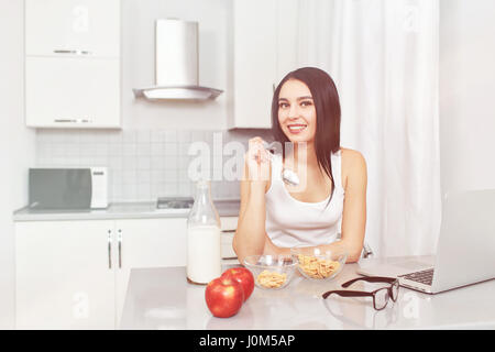 Eine junge Frau bereitet ein Diätfrühstück auf Rezept beim betrachten ihren Laptop. Ernährung, Äpfel, Müsli, Cornflakes - das Konzept der ein hea Stockfoto