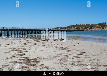 Menschen zu Fuß entlang der Victor Harbor Mole, die sich im Wasser spiegelt. Blick auf Granite Island bei Ebbe, Fleurieu Peninsula, South Au Stockfoto