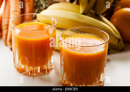 Glas Fruchtsaft mit Orangen, Karotten und Bananen auf einem Tisch Stockfoto