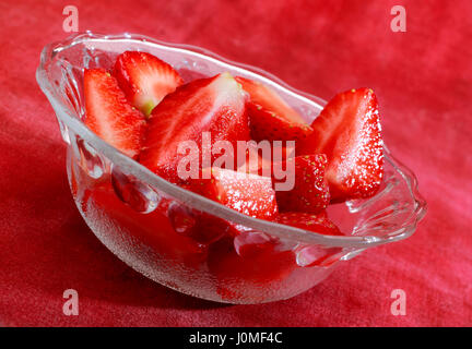Frische Erdbeeren in Glasschüssel auf rot Textil Hintergrund. Schrägen Gestell. Stockfoto