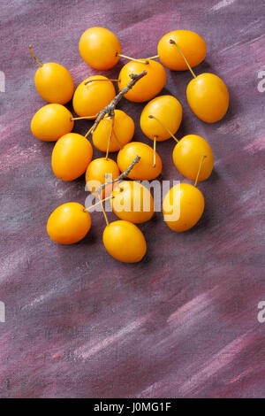 Gelbe Pflaume Mirabelle Früchte über bemalte Textilien Hintergrund. Draufsicht. Stockfoto