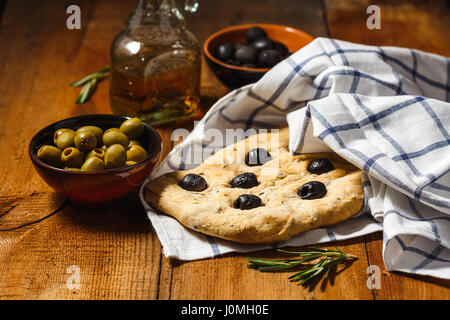 Traditionelle italienische Focaccia mit Oliven und Rosmarin mit Olivenöl auf Holztisch Stockfoto