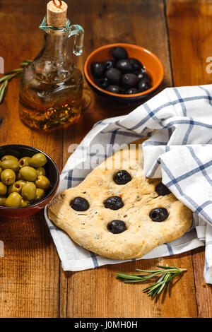 Traditionelle italienische Focaccia mit Oliven und Rosmarin mit Olivenöl auf Holztisch Stockfoto