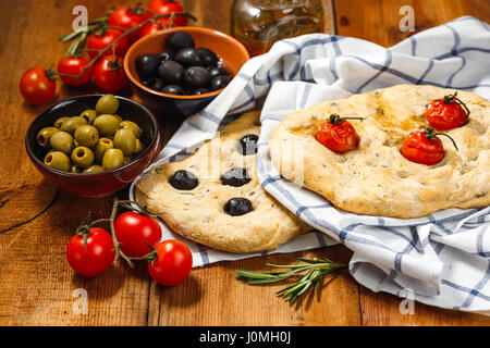 Traditionelle italienische Focaccia mit Tomaten und Oliven und Rosmarin mit Olivenöl auf Holztisch Stockfoto