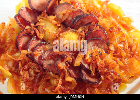 Die Nahaufnahme auf gebraten die Zwiebel Stücke, die Kartoffeln Scheiben und die Scheiben Wurst, geröstet in hitzebeständigen Glasgefäß. Ansicht von oben. Stockfoto