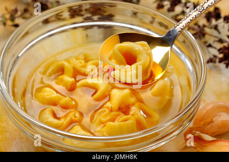 Frisch gekochte Tortellini in Glasschale mit Brühe. Einzelne Tortellini auf Löffel. Stockfoto