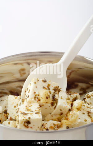 Die Nahaufnahme auf Blöcke von Feta-Käse mit Kräutern und Knoblauch mit Olivenöl mit Plastiklöffel in Stahl Gericht angeordnet. Kopieren Sie Leerzeichen am Anfang der Foto. Stockfoto